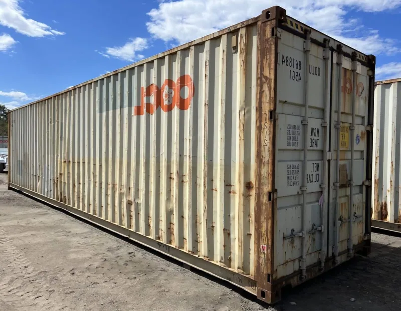 Weathered white 12m shipping container with faded third-party markings, standing in a container yard