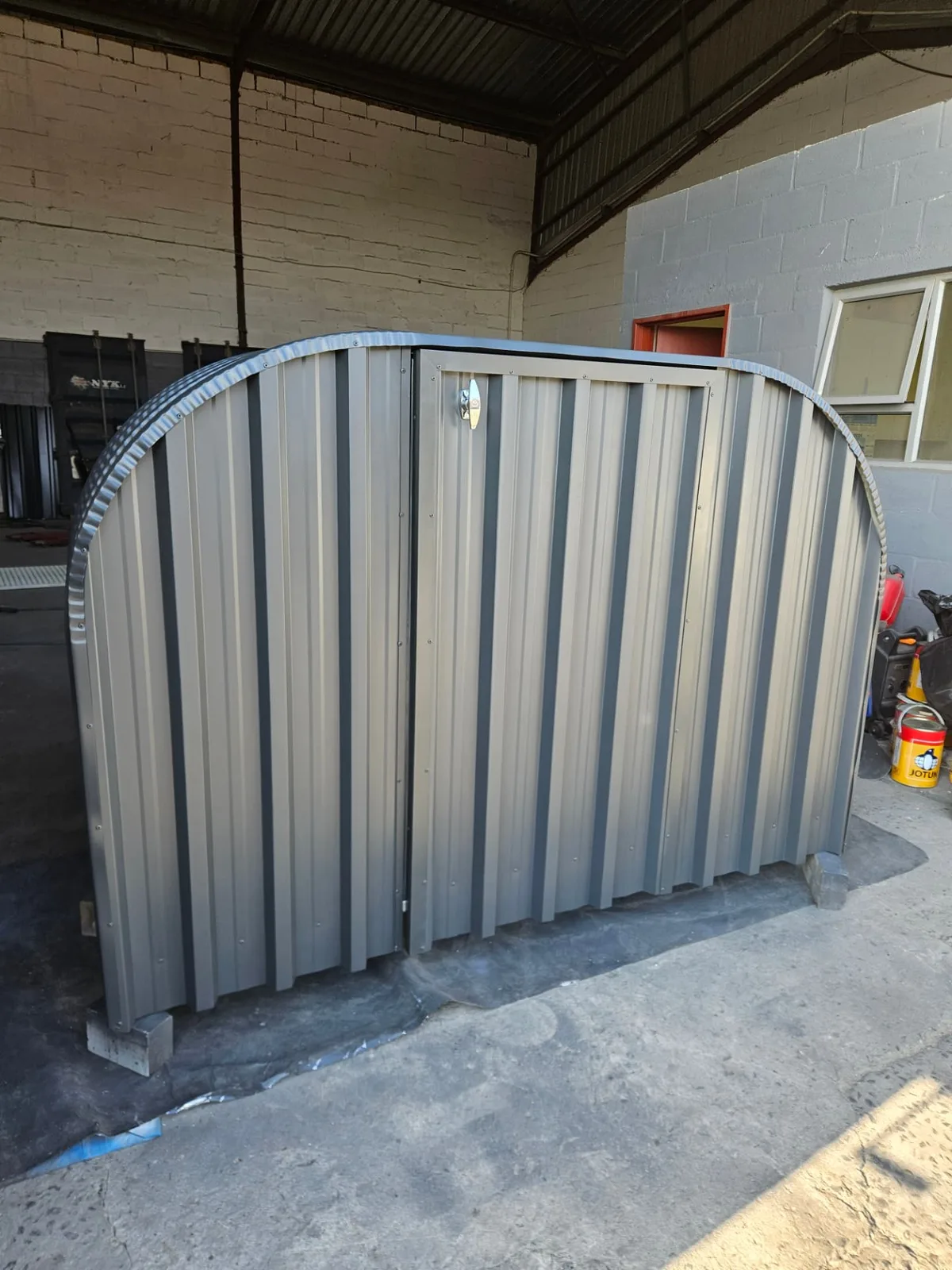 Firewood shed with both corrugated steel doors closed and a stainless latch fitted