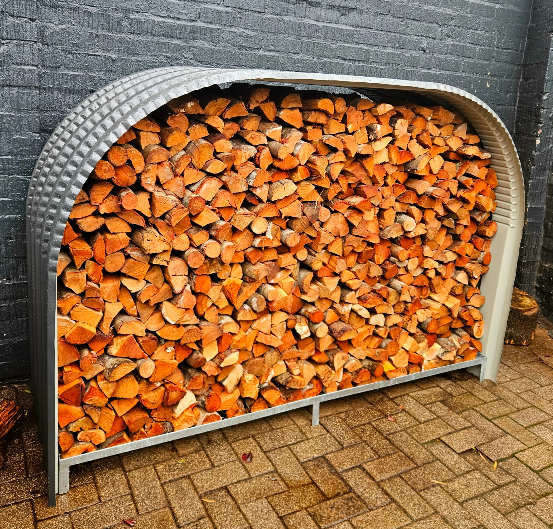 Firewood shed fully packed with freshly split logs against a grey painted brick wall