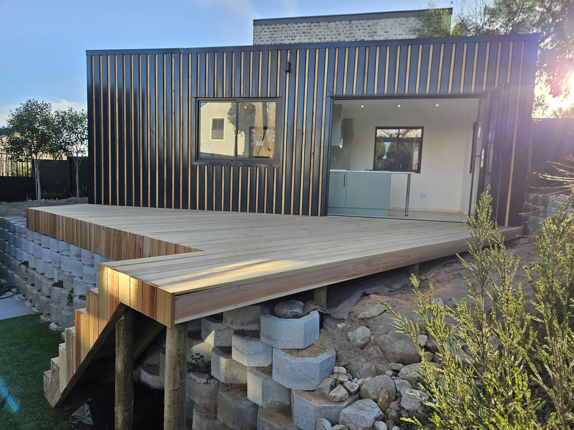 Modular home clad in vertical timber and steel with a timber deck built over a concrete block retaining wall