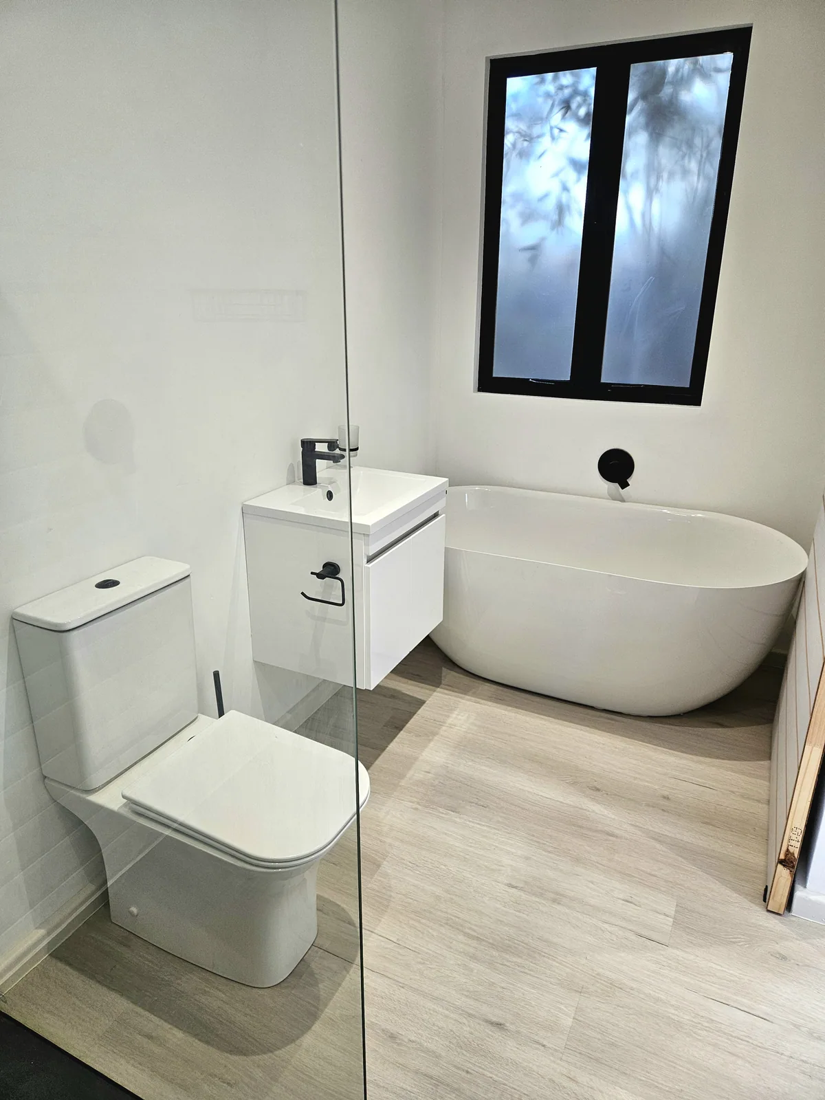 One Bedroom Pod bathroom viewed toward the freestanding bath, wall-hung basin and black-framed window