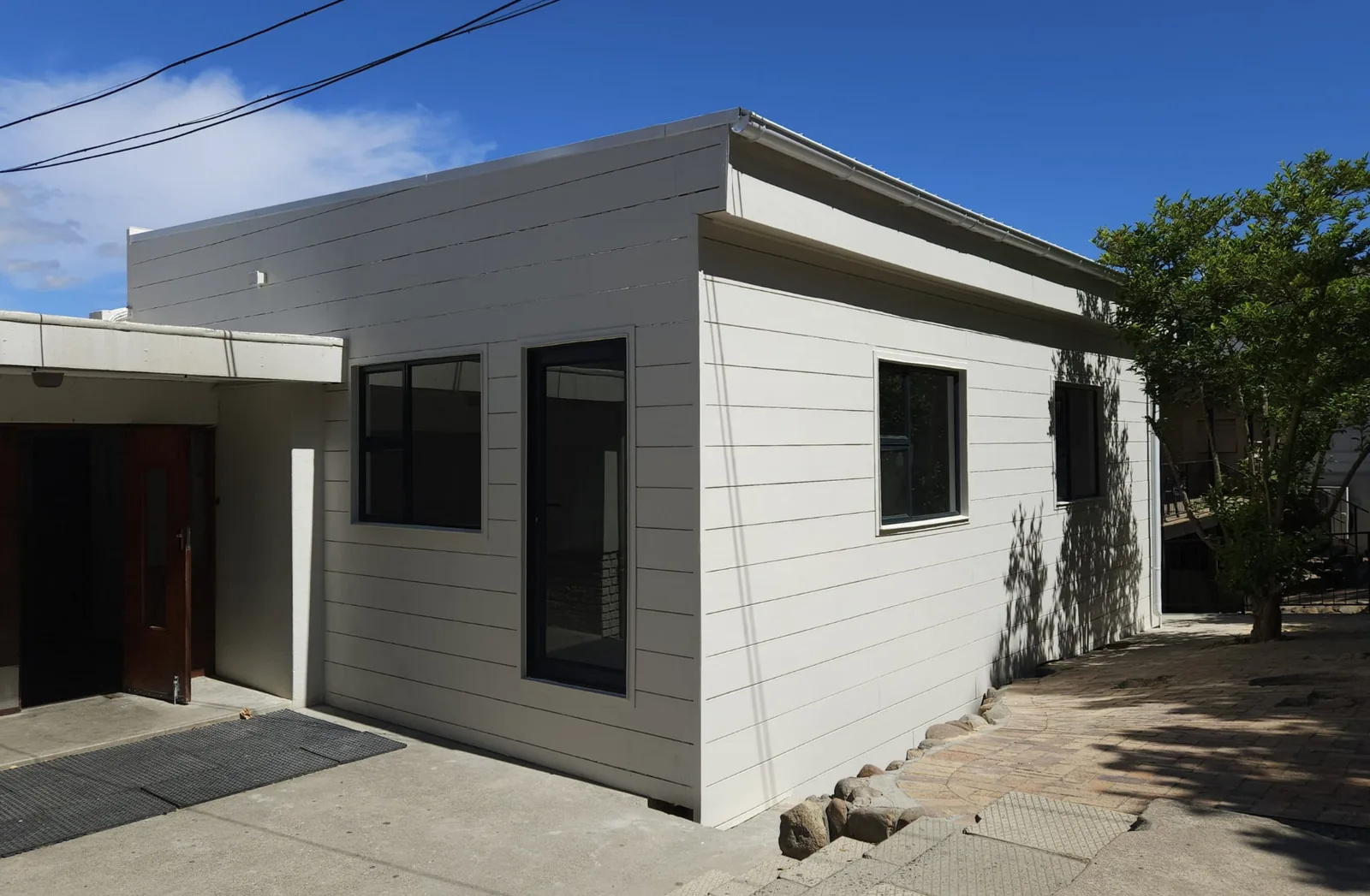Completed art classroom exterior with fibre-cement cladding, dark aluminium door and windows, alongside the existing school building