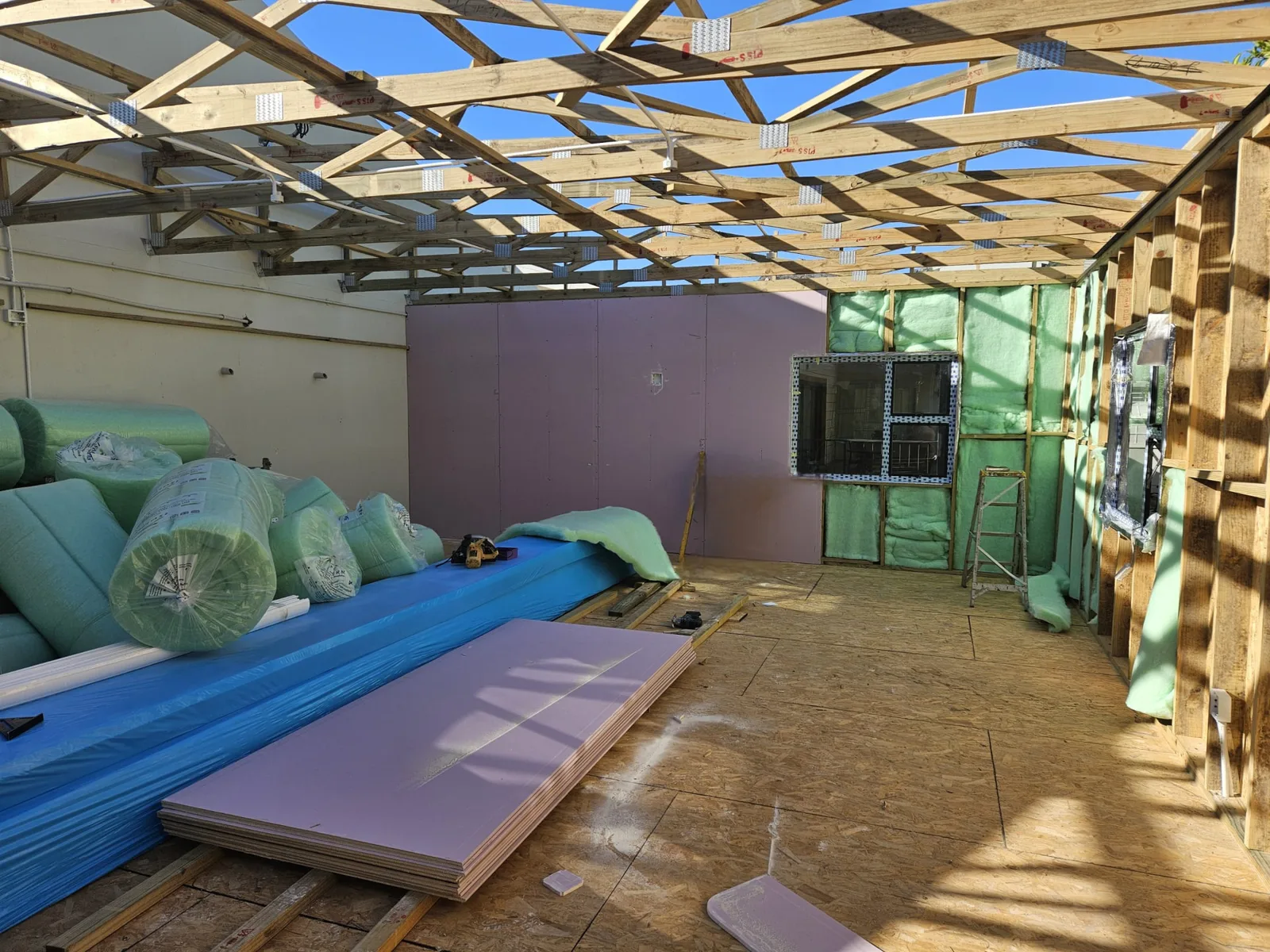 Interior during construction with roof trusses in place and wall insulation being installed