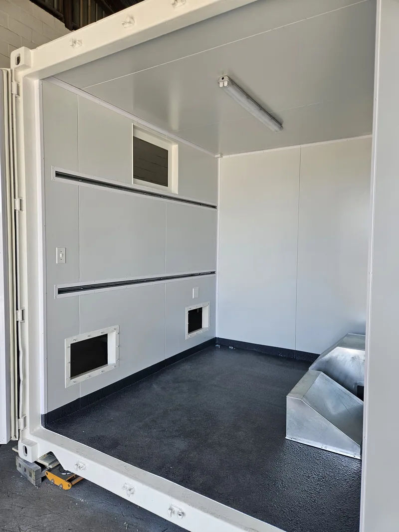 Corner view inside a white-panelled container with an open door leaf, insulated ceiling and grey floor