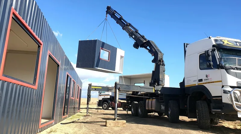 Truck-mounted crane lifting a module into position alongside the completed classroom block during installation