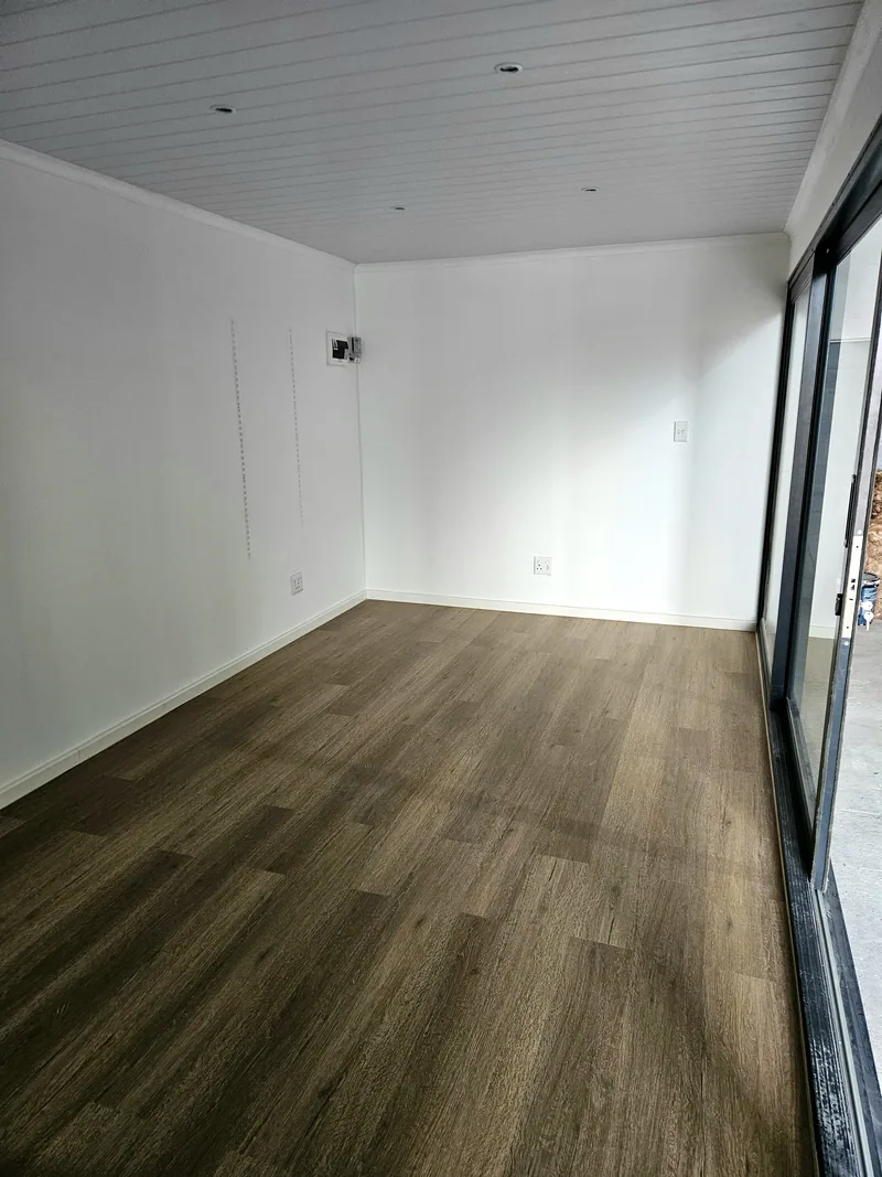 Empty interior with white walls, a white ceiling and dark wood-look flooring beside sliding glass doors