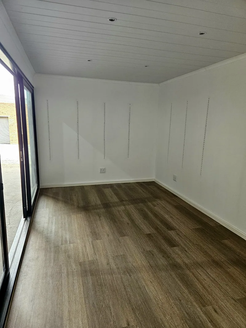 Corner of an empty fit-out with white panelled walls and wood-look flooring next to glazed sliding doors