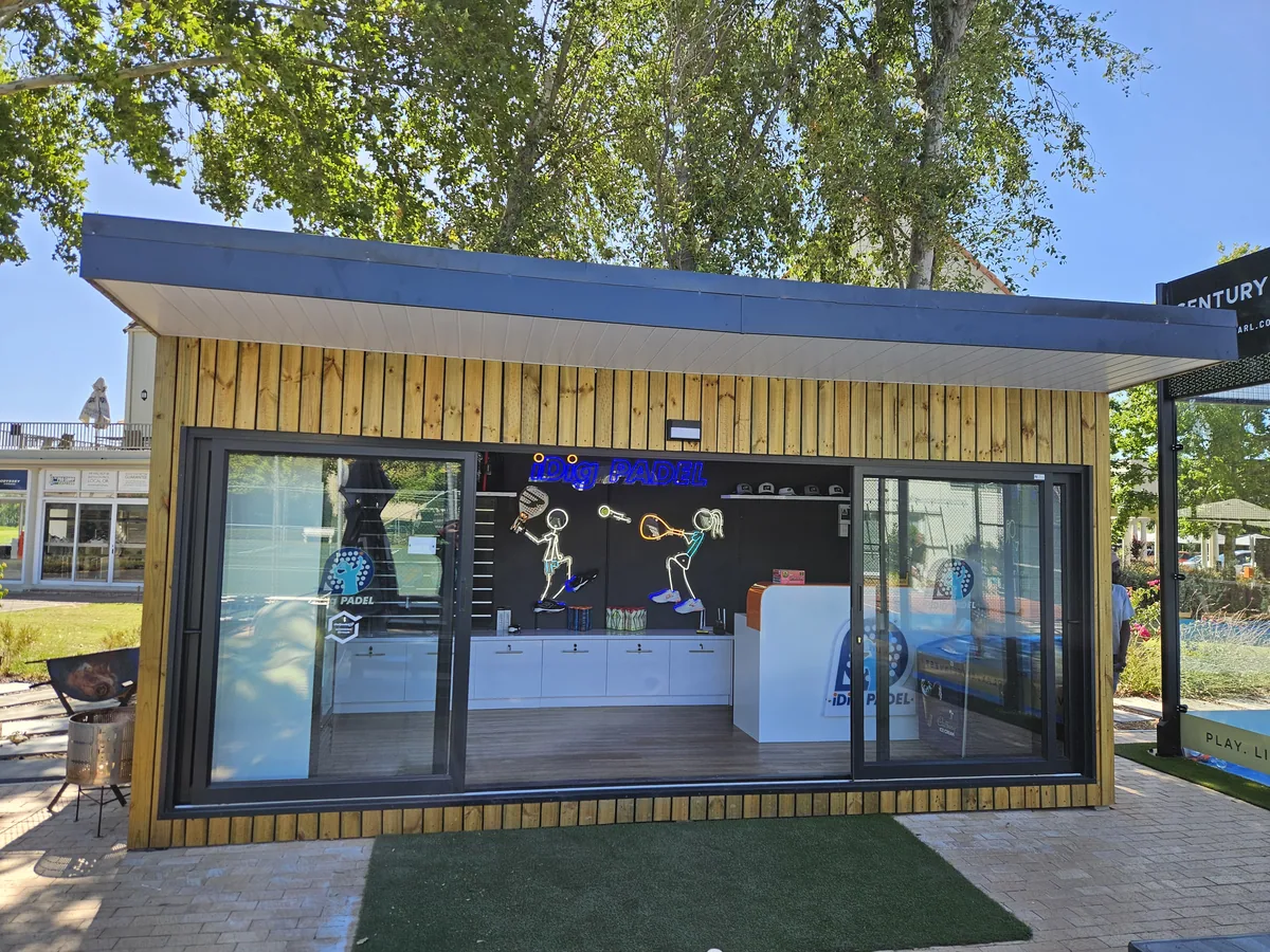 Illuminated timber-clad pro shop at dusk with glazed frontage, retail displays and branded signage inside