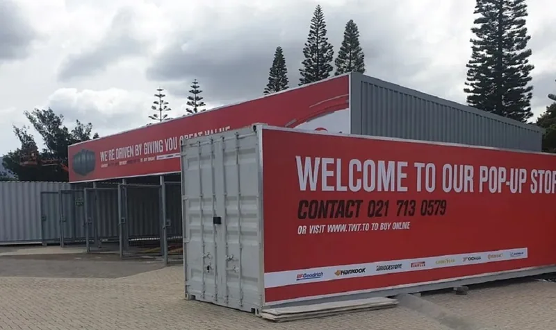 Container pop-up store exterior with red branded banners and a plain container in the foreground