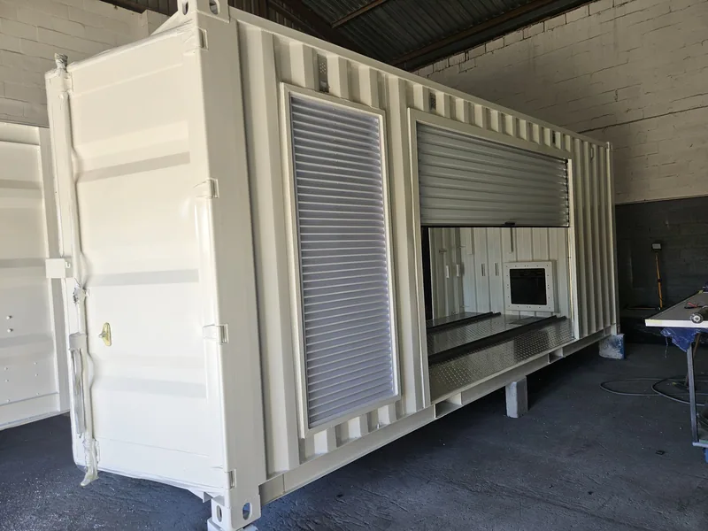 Two white containers side by side in a workshop with roller shutter doors and hatch openings