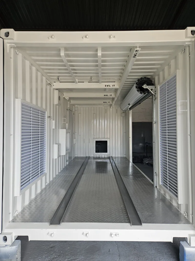 Long interior of a white-lined container with a floor channel, wall vents and a fan at the far end