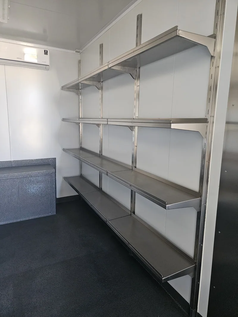 Row of stainless steel wall shelves inside a white-lined container with a strip light overhead
